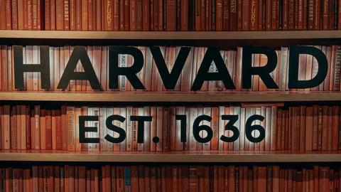 Bookshelf with overlaid digital lettering: "Harvard est. 1636"